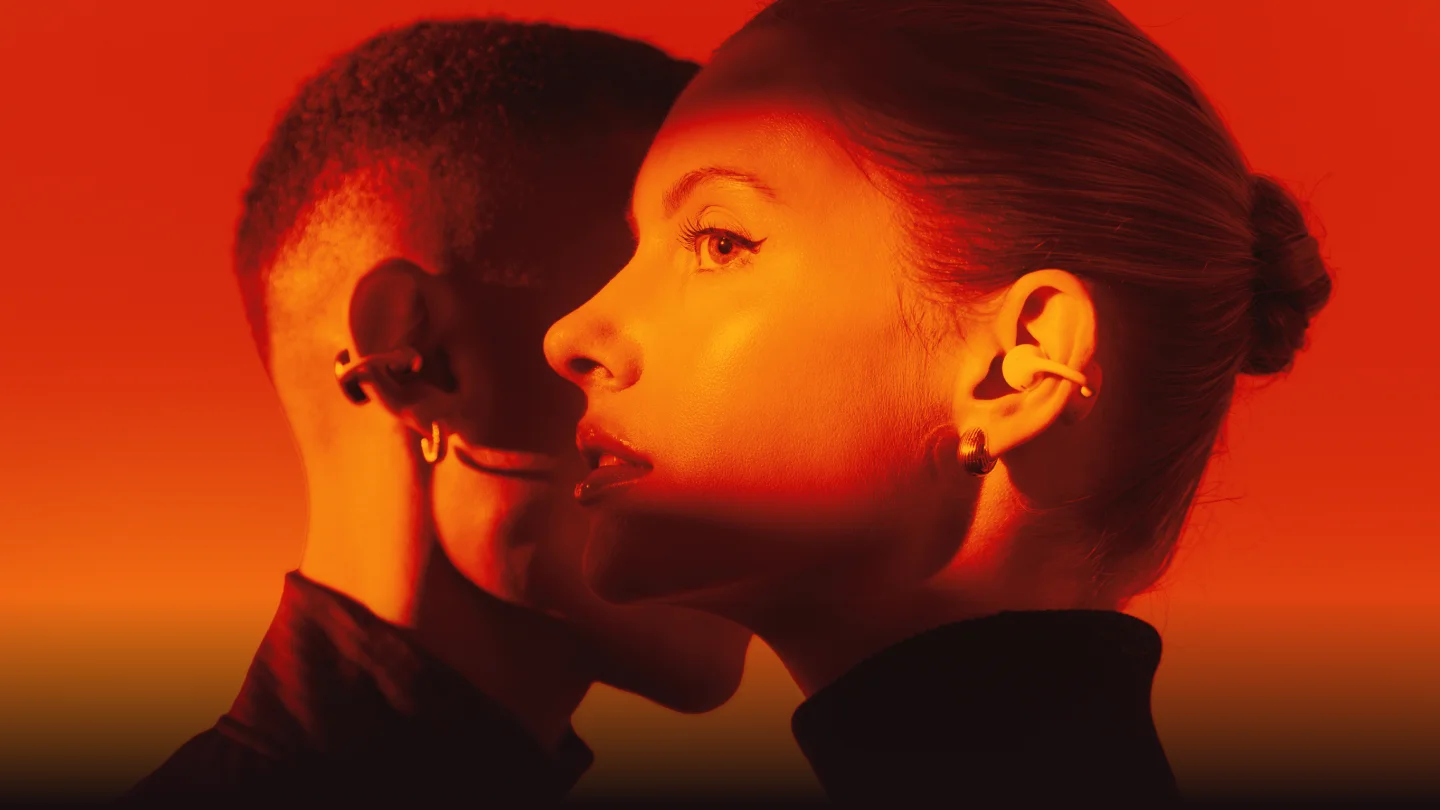 Two people wearing HiClips open-ear earphones in warm orange lighting Two people wearing HiClips open-ear earphones in warm orange lighting